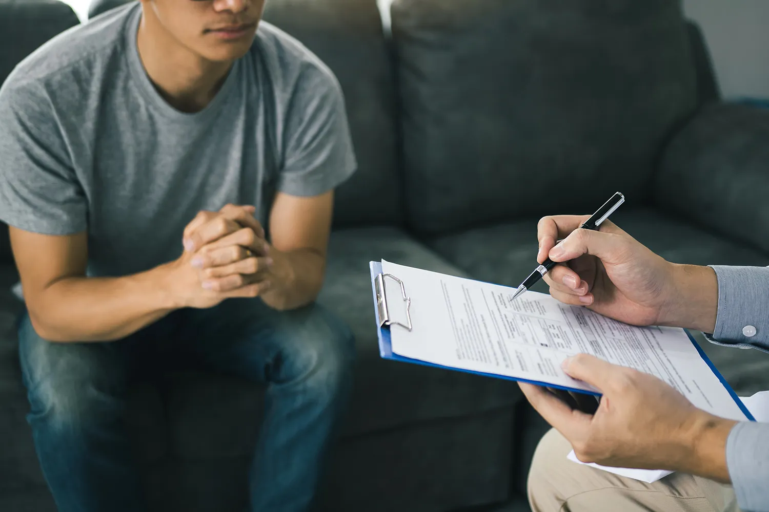 Provider filling out an intake form on a clipboard while a patient waits on a couch.