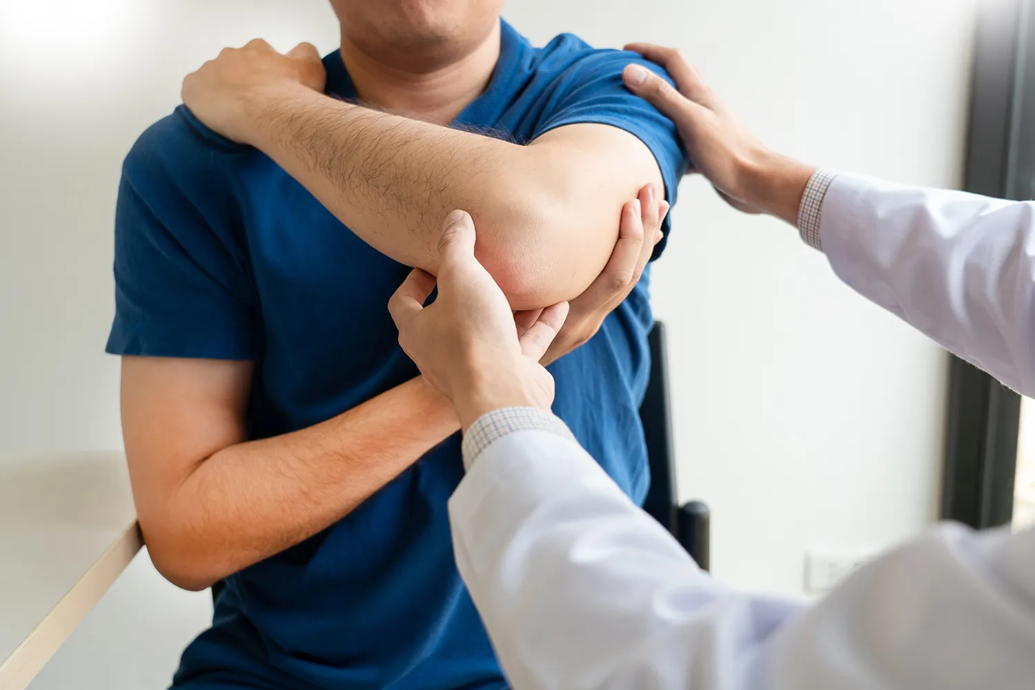 Provider in a white coat examining a man’s elbow and shoulder.