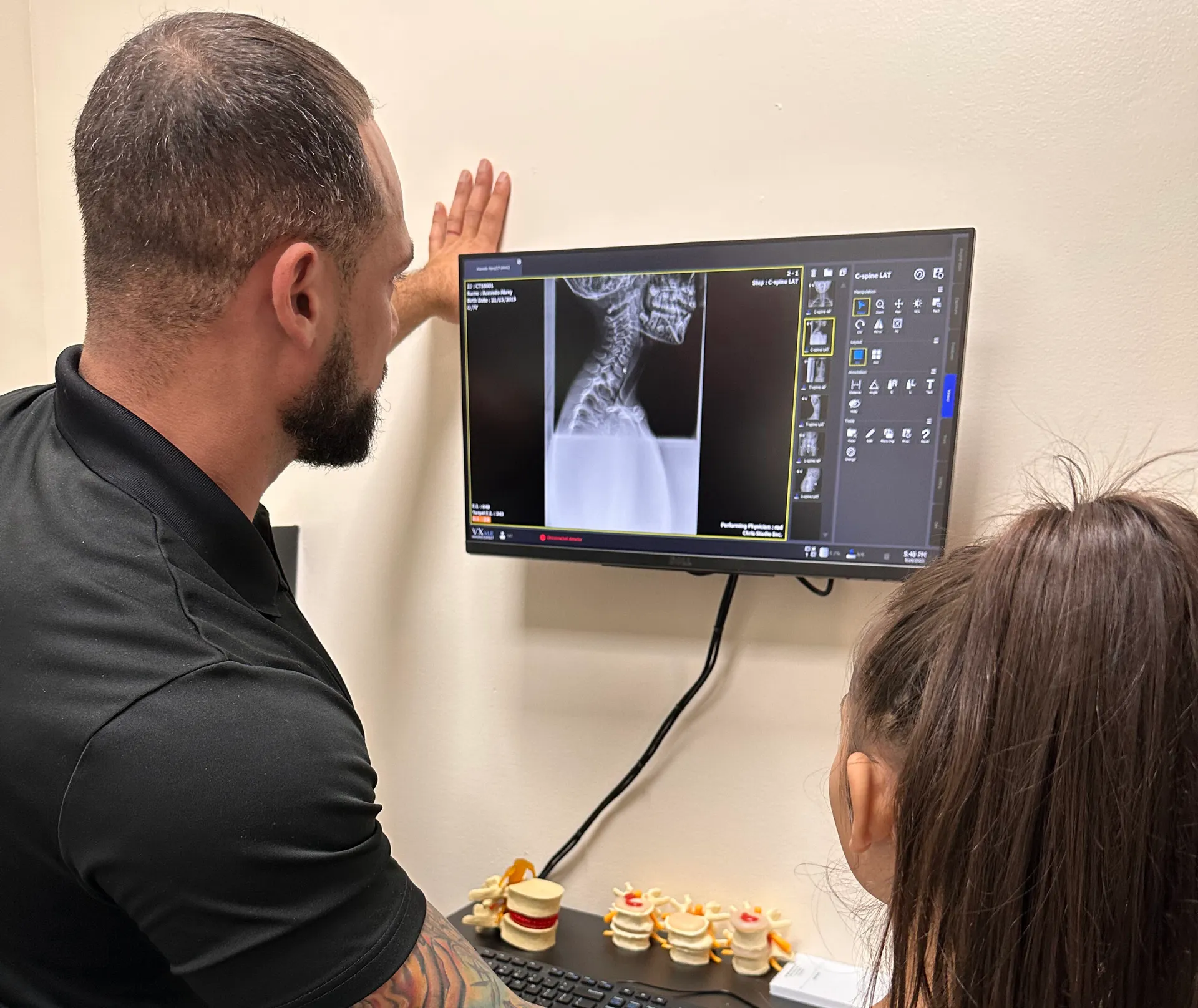 Dr. Junior showing a girl a neck X-ray on a wall-mounted monitor.