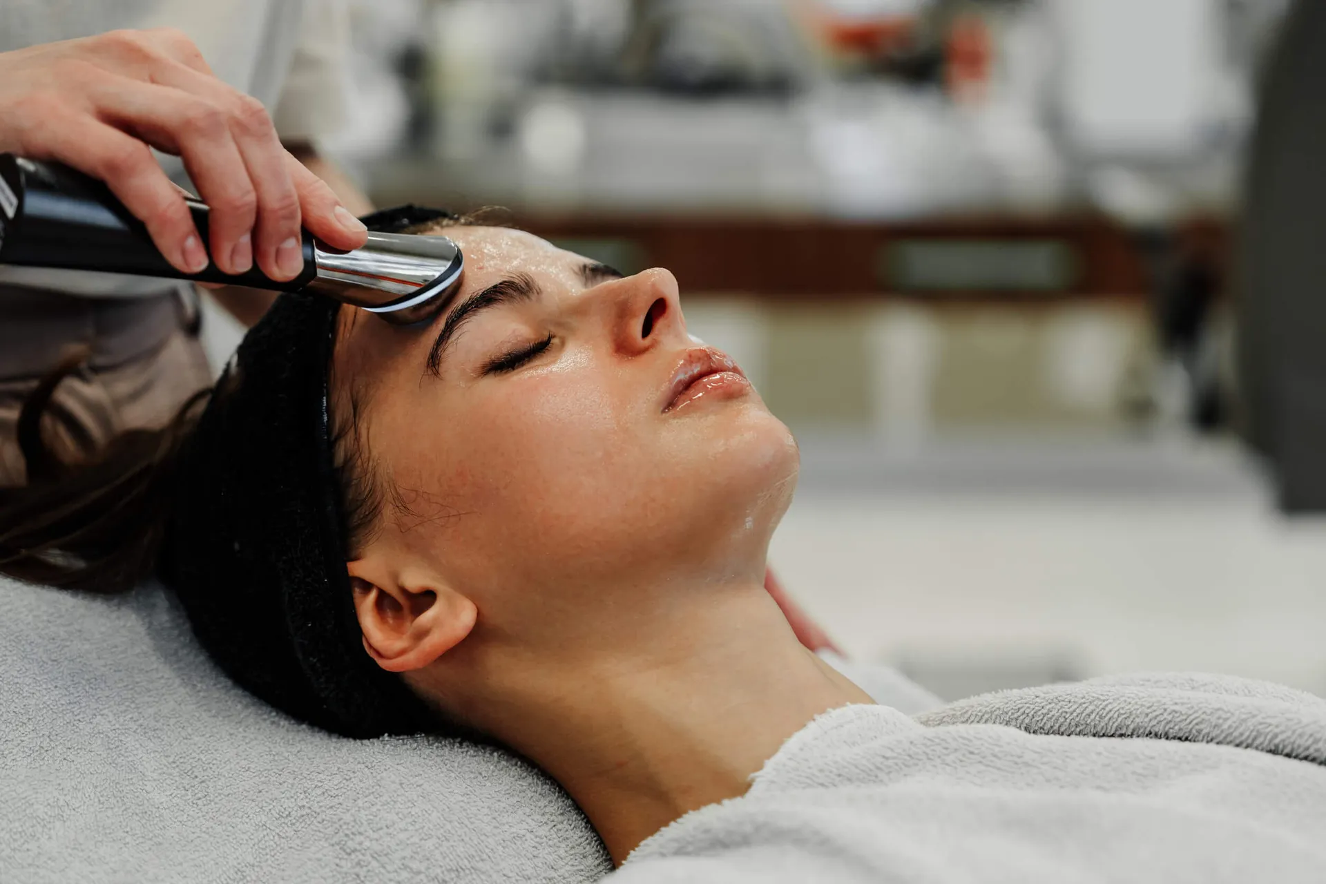 Woman with eyes closed receiving a facial treatment with a handheld device on her forehead.
