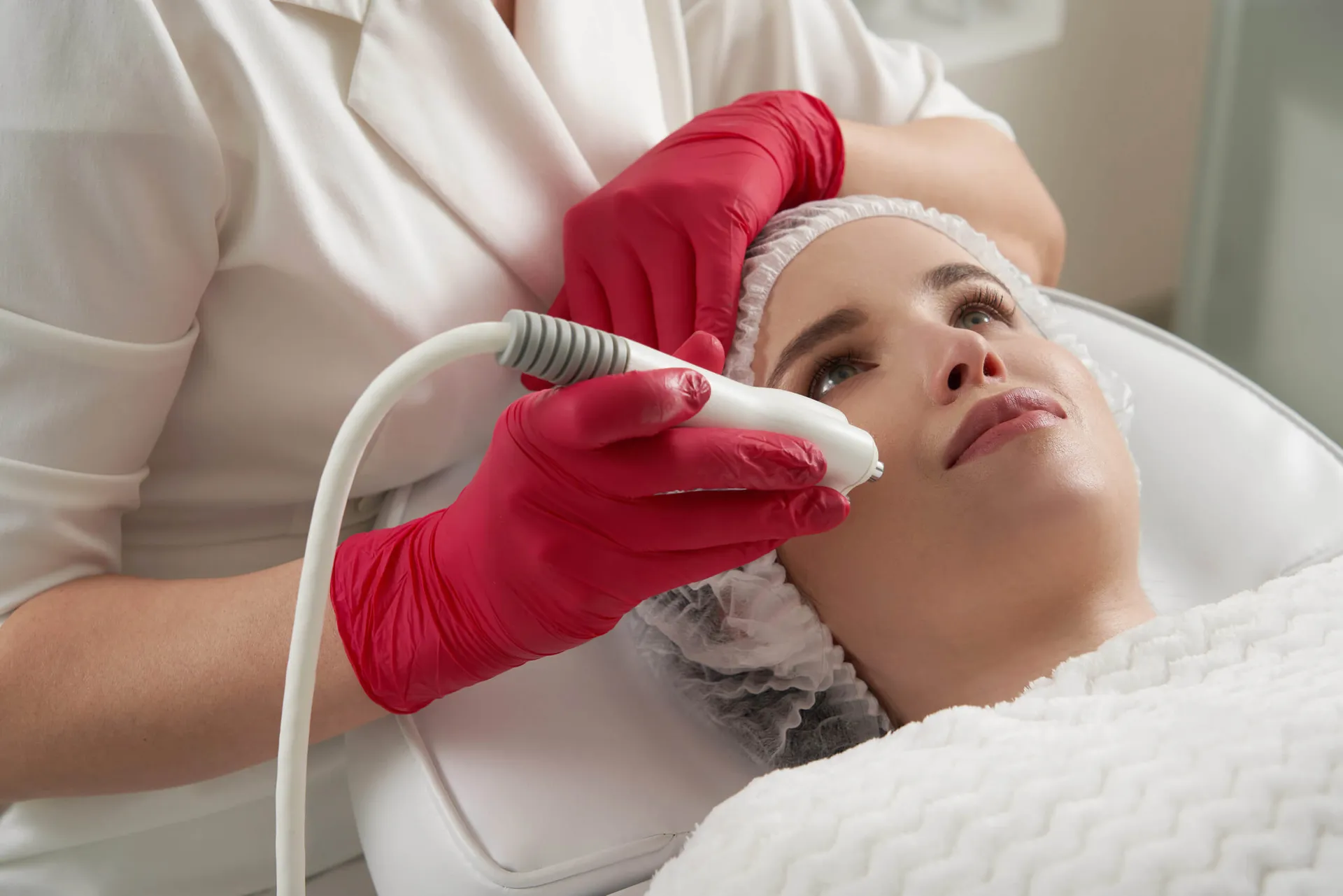 Woman lying back as a technician in red gloves applies a handheld device to her face.