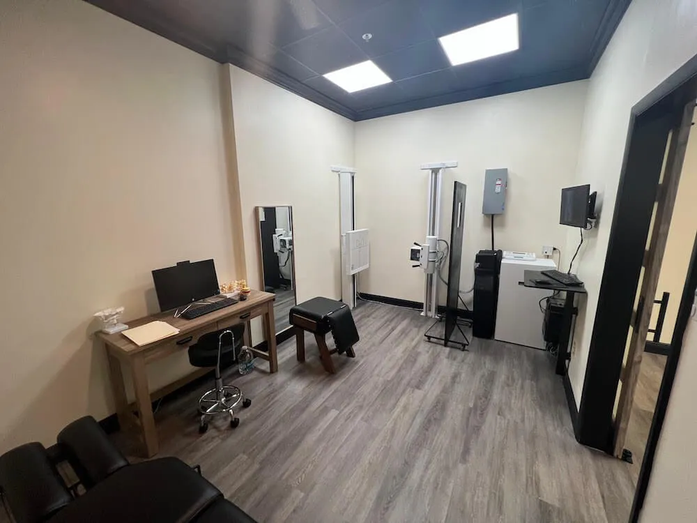 Chiro Studio X-ray room with a digital X-ray unit, a computer desk, and monitors.