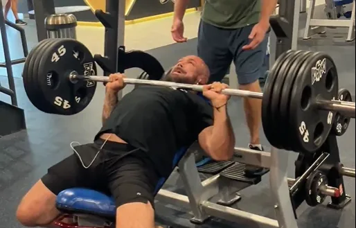Dr. Junior bench pressing a loaded barbell while a spotter stands behind him.