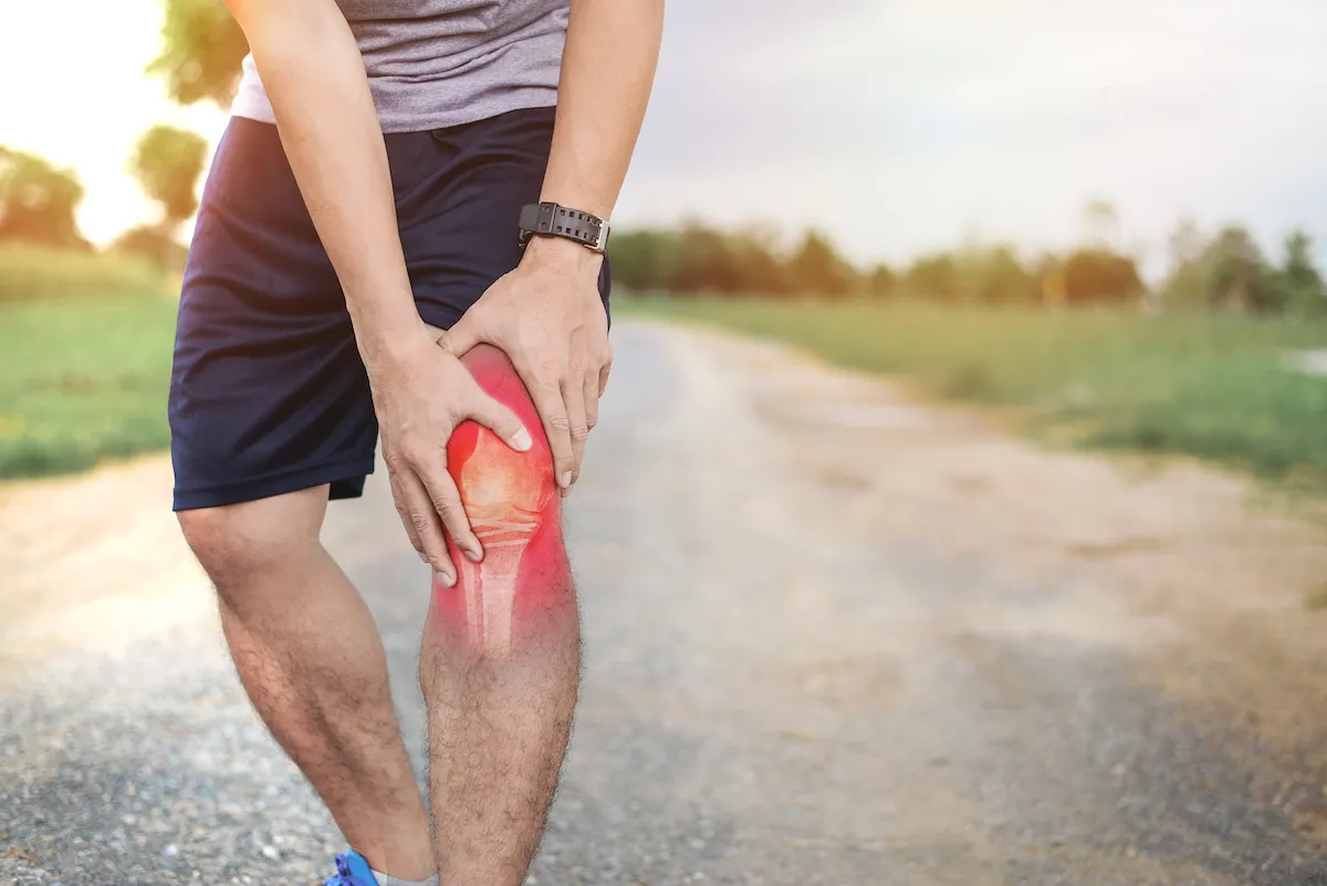 Runner on a trail holding his knee, with the knee joint highlighted in red.