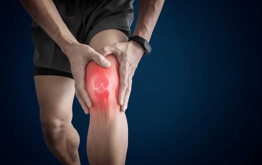 Athlete gripping his knee, with the knee joint highlighted in red.