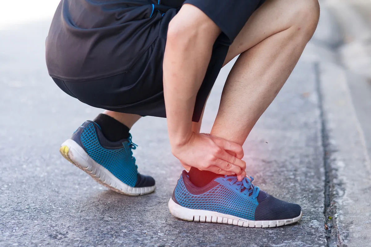 Runner crouching on the pavement holding a sprained ankle.